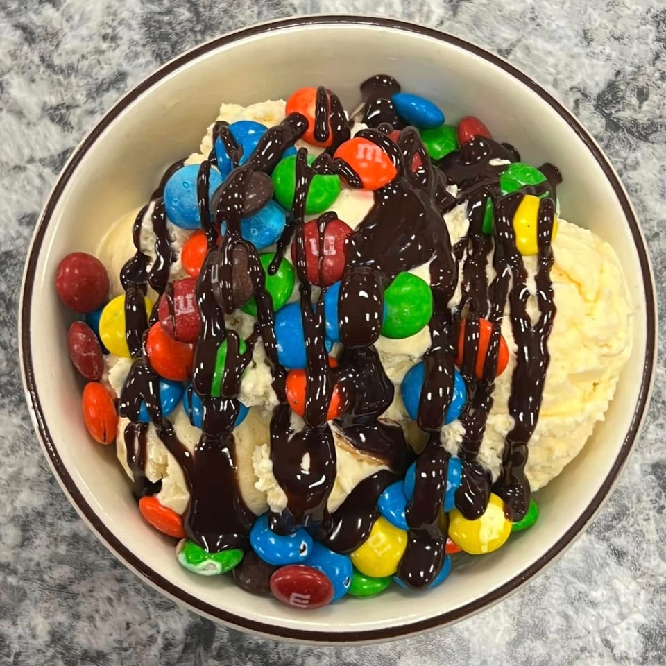 Vanilla ice cream topped with colorful M&M's and drizzled with chocolate syrup in a white bowl.