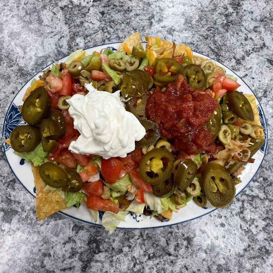 A large plate of nachos with sour cream, salsa, jalapeños, olives, lettuce, and tomatoes.