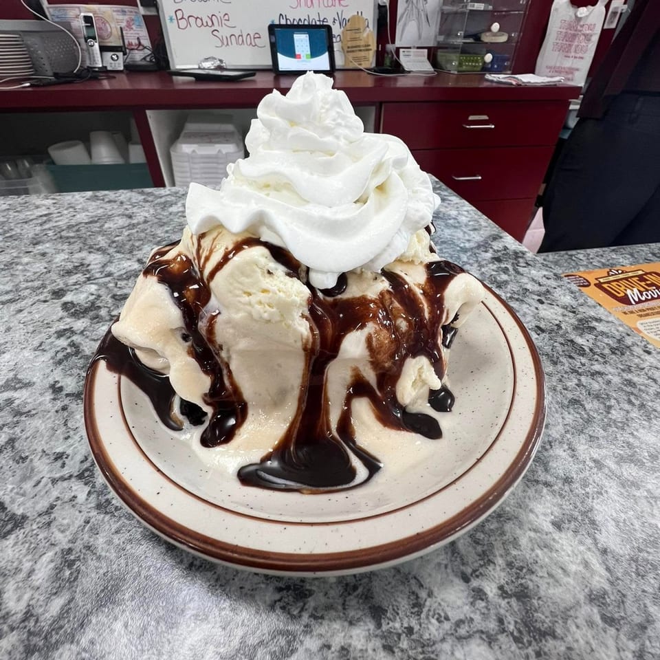 A vanilla ice cream sundae with chocolate syrup and whipped cream on a diner counter.