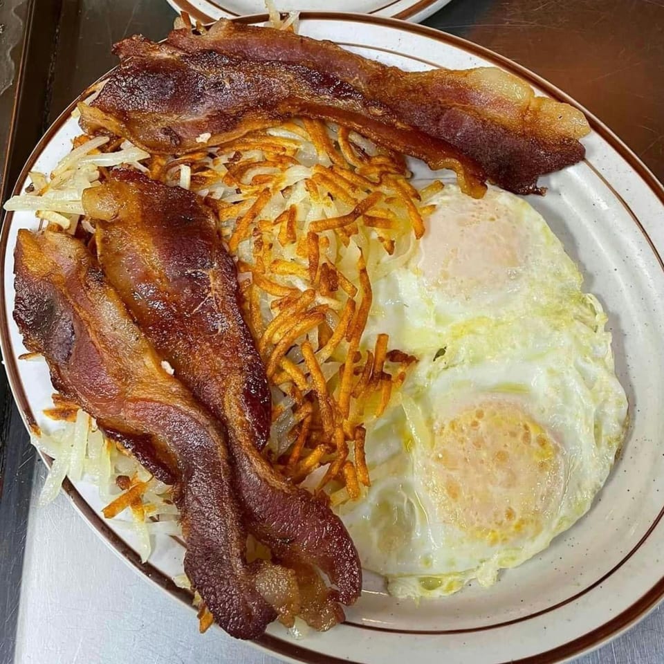 A breakfast plate with crispy bacon, golden hash browns, and two fried eggs.