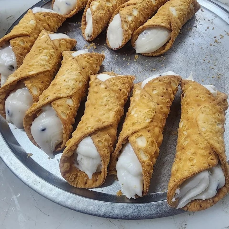 A silver tray filled with several golden-brown cannolis, generously stuffed with white cream filling.