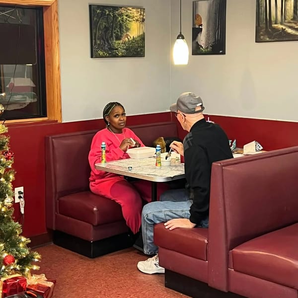 Two diners, a woman and a man, seated in red booths at a table in Broadway FAMILY Grill.