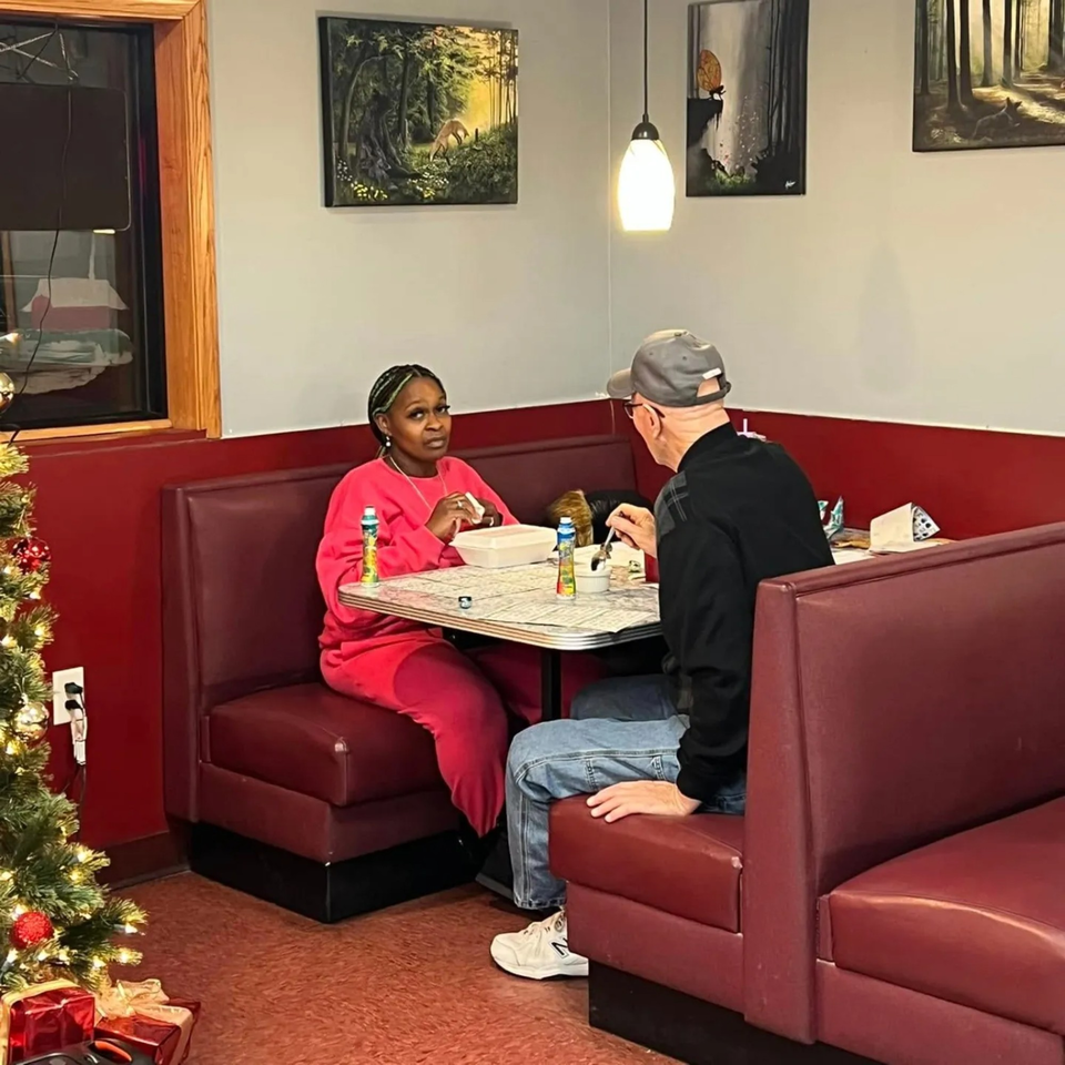 Two diners, a woman and a man, seated in red booths at a table in Broadway FAMILY Grill.