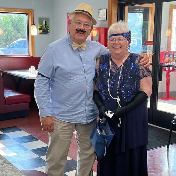 A man and woman in 1920s-themed costumes pose inside Broadway FAMILY Grill.
