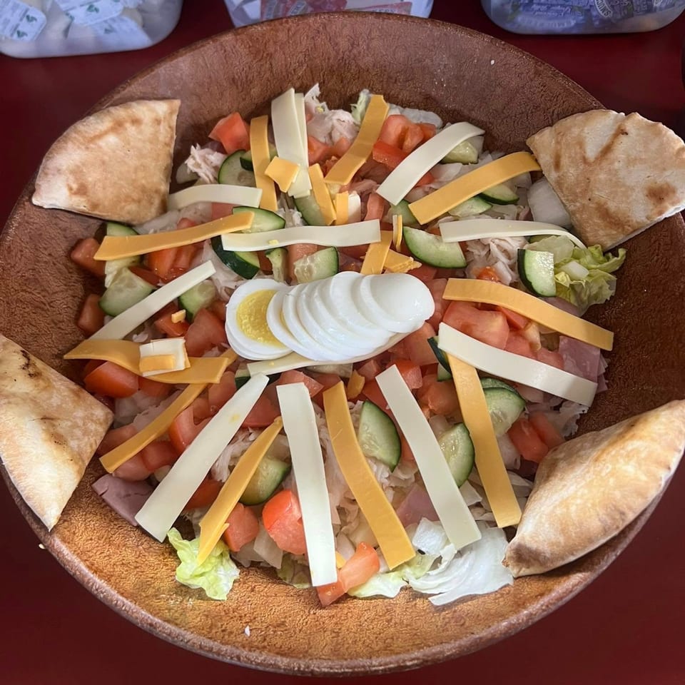 A large American chef salad with pita bread, cheese, tomatoes, cucumbers, and sliced egg.