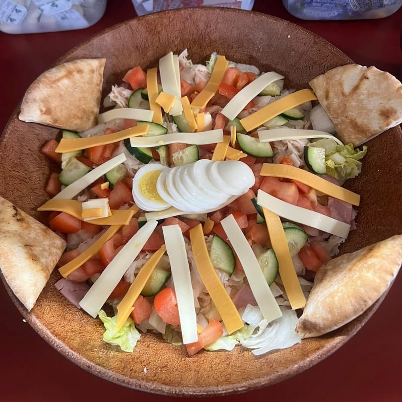 A large American chef salad with pita bread, cheese, tomatoes, cucumbers, and sliced egg.